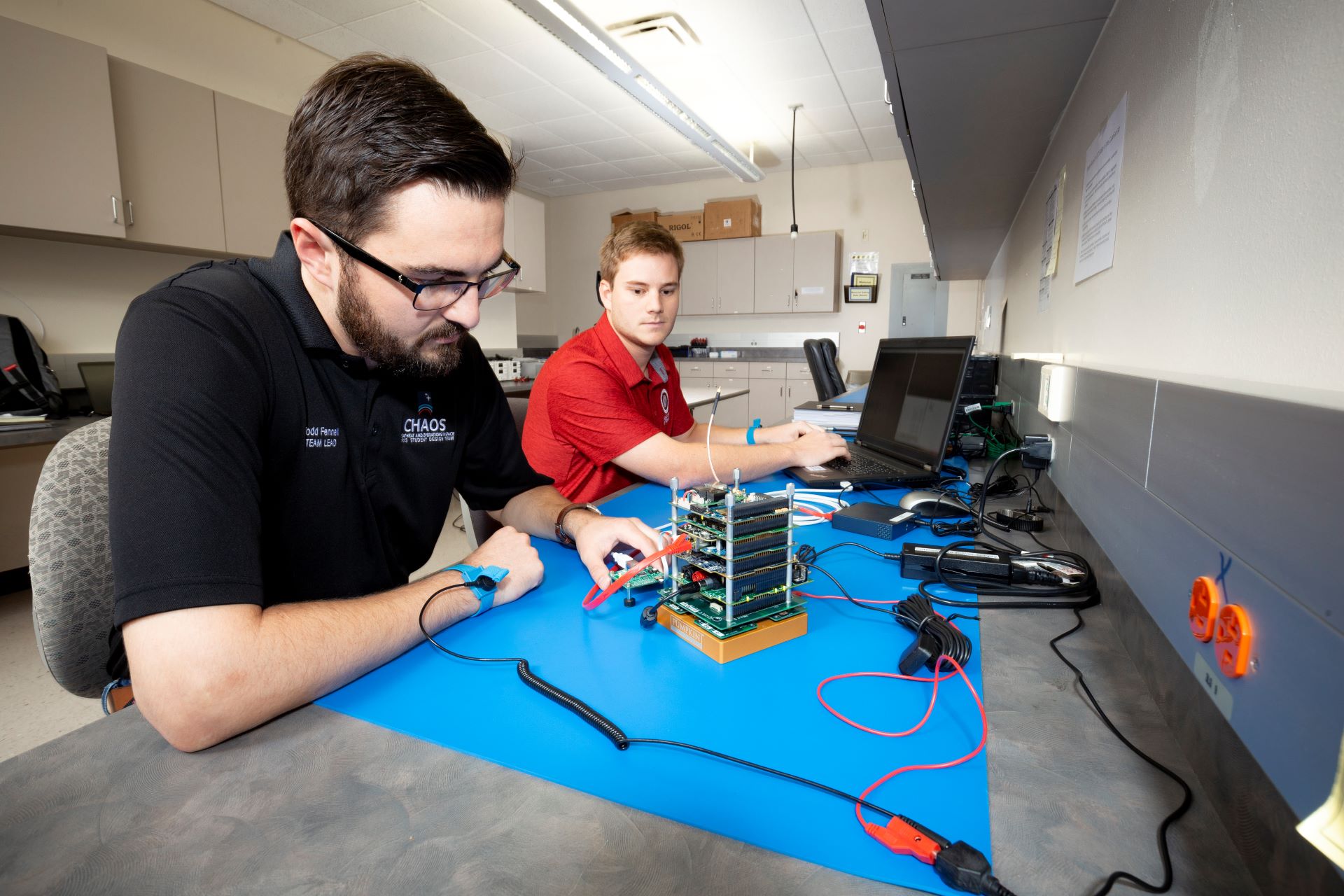 Two students collaborating on a project, one holding a hard drive and the other sitting at a computer